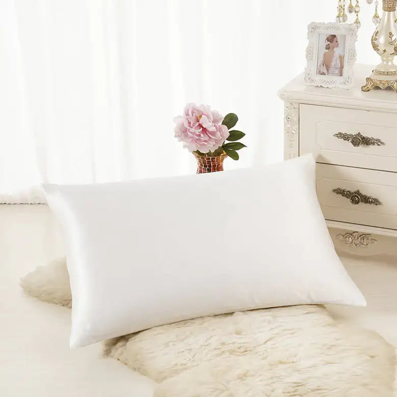 Luxurious white silk pillowcase displayed on soft rug in elegant bedroom setting.