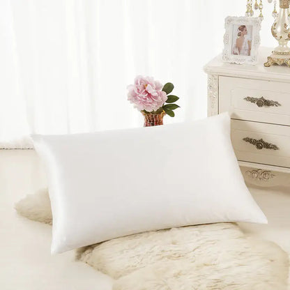 Luxurious white silk pillowcase displayed on soft rug in elegant bedroom setting.