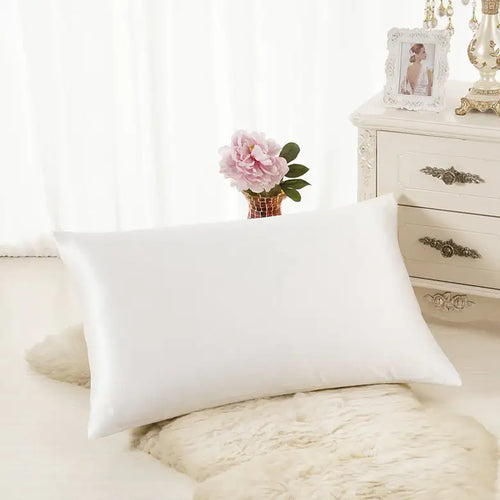 Luxurious white silk pillowcase displayed on soft rug in elegant bedroom setting.